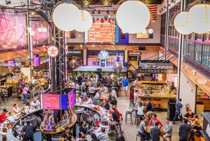 Overlooking the circular bar and tables inside The Market, where the tall ceiling and bright globe lights provide a warm atmosphere.