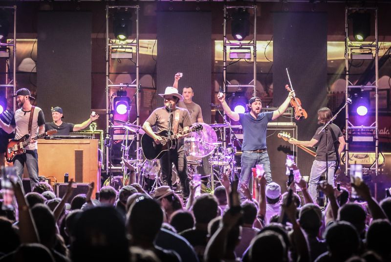 The audience cheers as the band on stage pauses to raise shot glasses in a toast to the crowd.