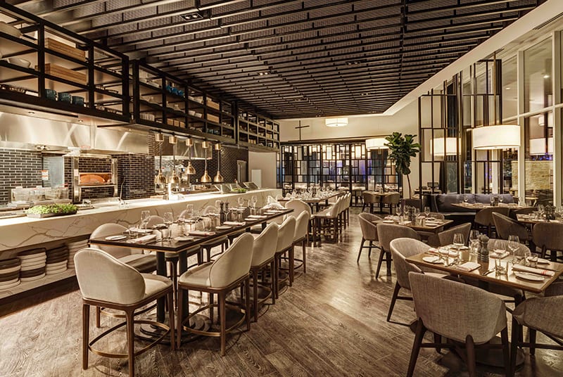 The Cut & Bourbon restaurant has a warm atmosphere, with modern gray wood floors, glass-pane walls and cozy dining chairs.