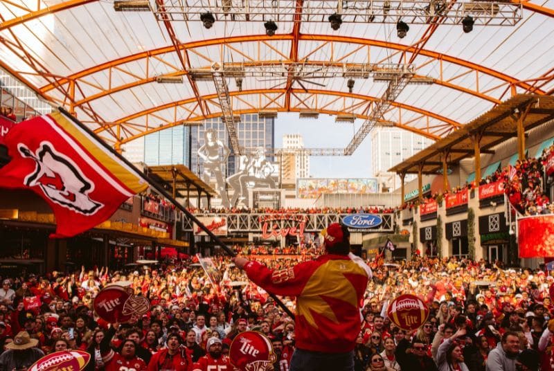 A passionate crowd cheers as a man waves a Kansas City Chiefs flag from the stage as the team plays for the AFC Championship!