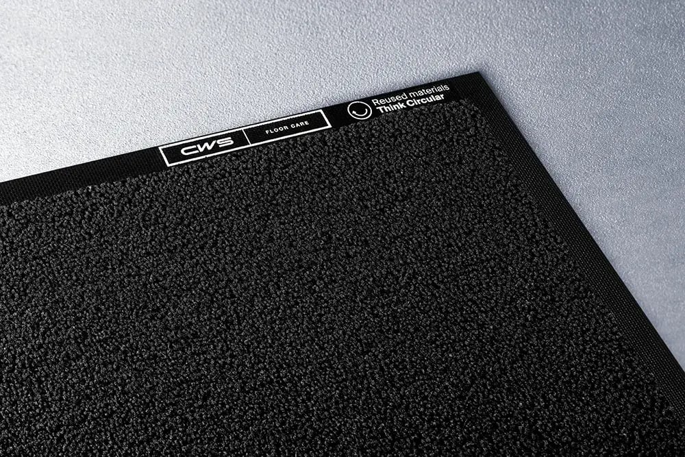 Black dust care mat from CWS Hygiene on light grey floor