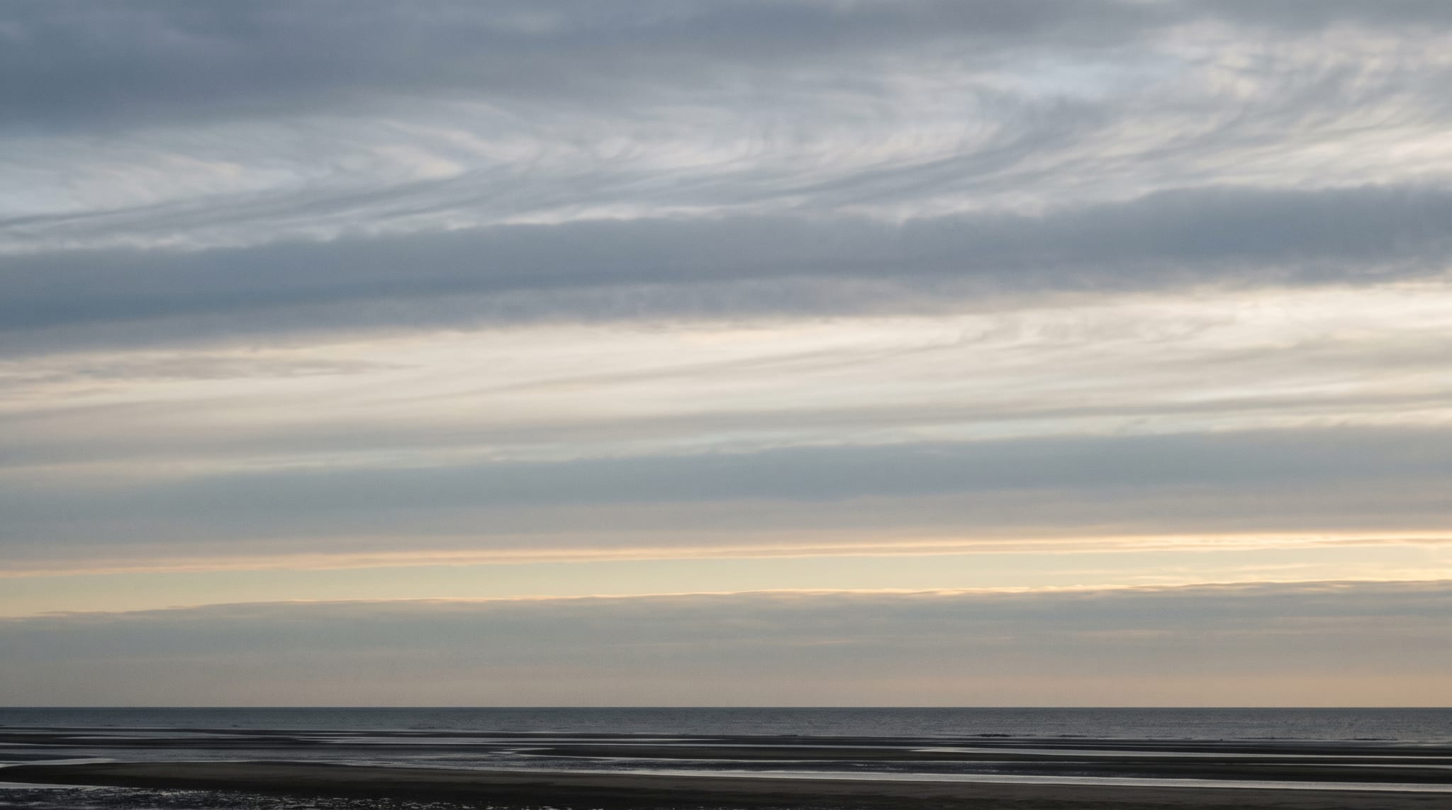 Layered high cloud over an empty coastline at first light