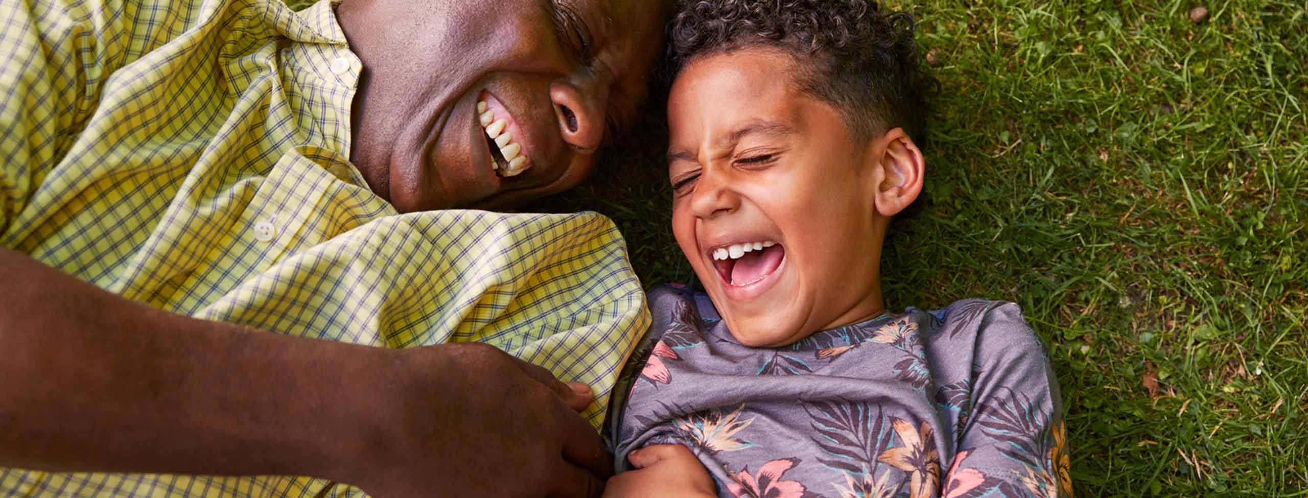 laughing boy and grandpa laying in grass 2