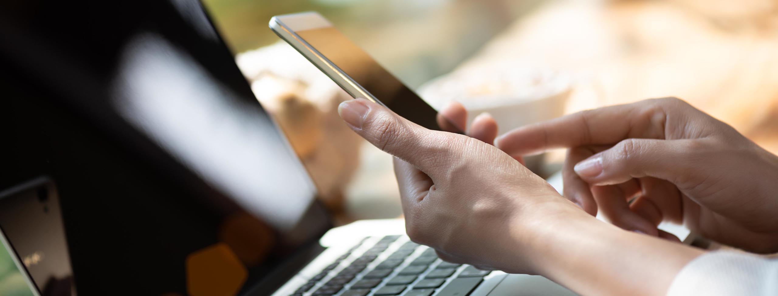 Woman holding white mobile phone with a laptop