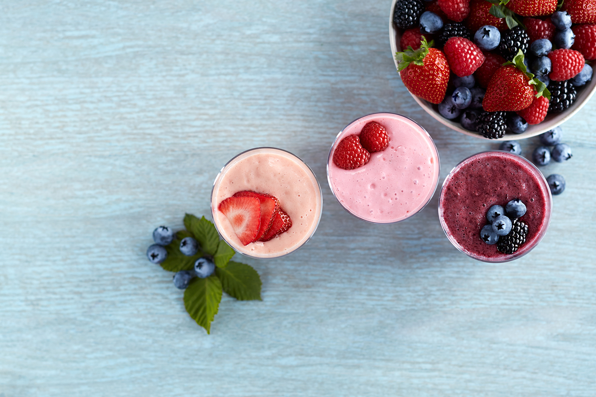 Three mixed berry smoothies next to a bowl of berries. 
