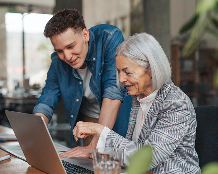 younger person helping older person with computer