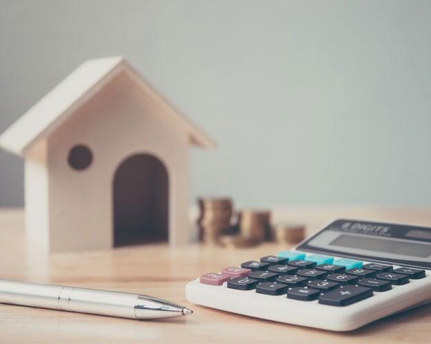 Calculator with wooden house and coins stack