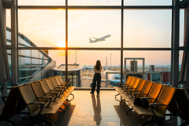 woman looking at a plane through an airport window 