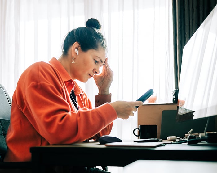 woman looking at phone while in front of a computer