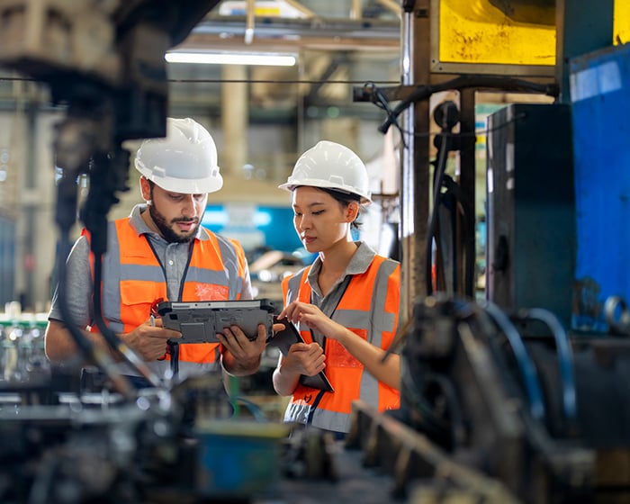 two manufacturing employees surrounded by equipment looking at a tablet