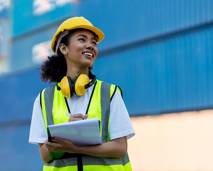 Woman in yellow safety gear, holding a clipboard