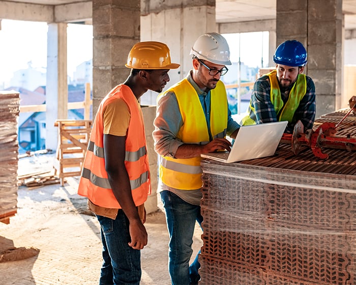 three construction workers looking at a laptop