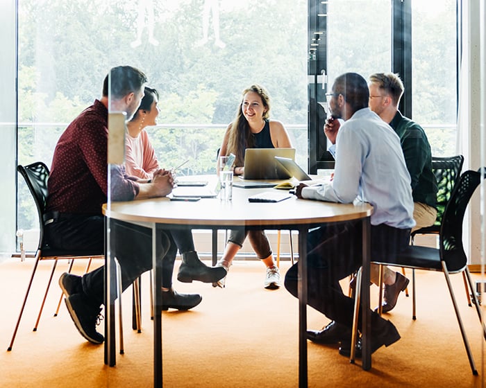 five men and women sitting around a table talking