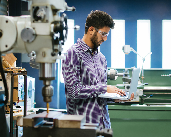 man working on laptop surrounded by manufacturing equipment