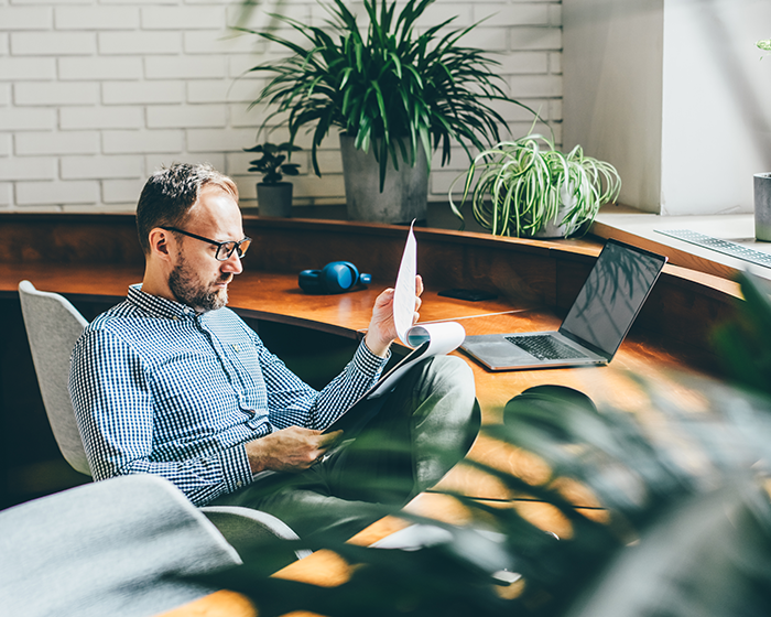 man reading papers in front of laptop