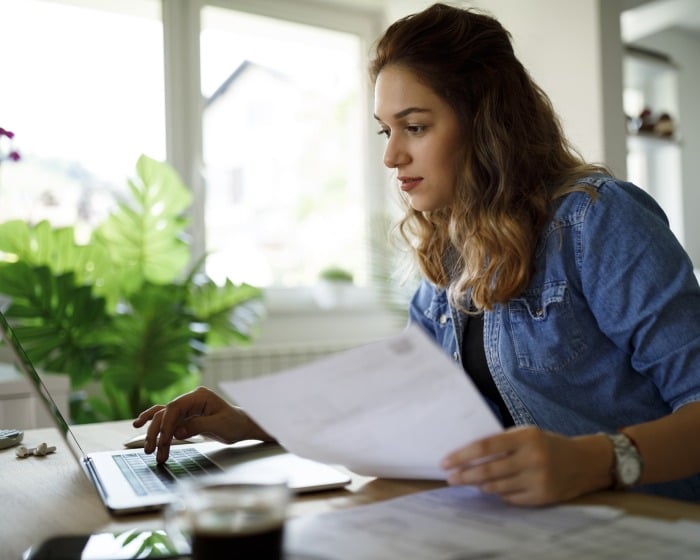 woman typing on a laptop while looking at a piece of paper