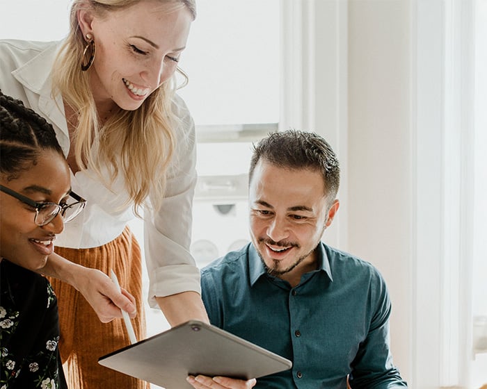Three coworkers smiling while looking at something on a tablet.