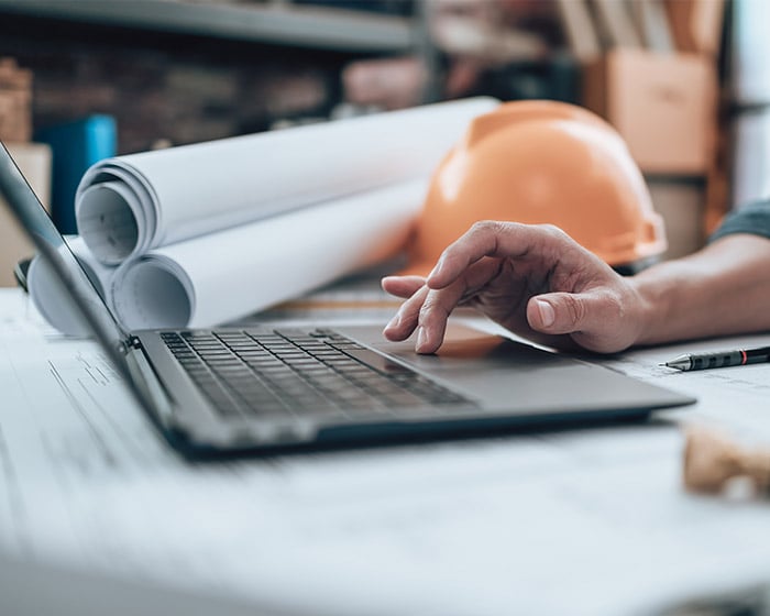 engineer working on computer with hard hat and blueprints in background