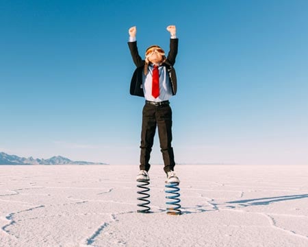 Young Boy Businessman Stands Arms Raised on Springs