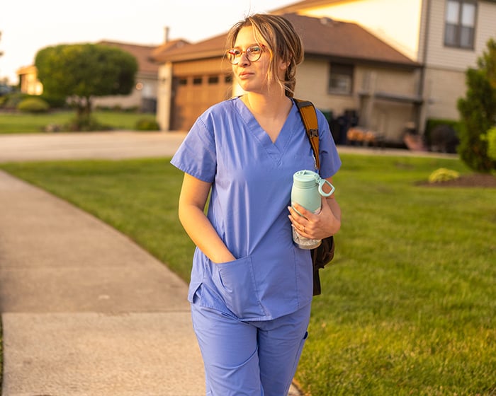 Woman in scrubs walking through a neighborhood