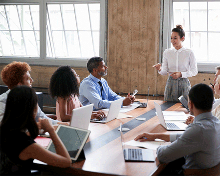 Female-manager-stands-addressing-team-at-board-meeting