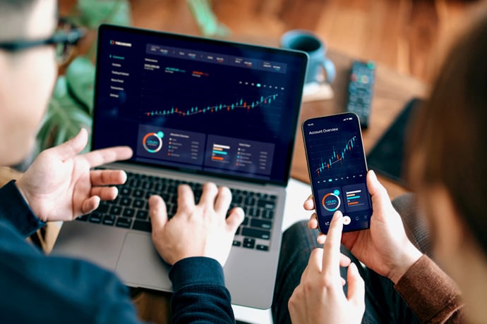 Two people looking at investments on their phone and computer.