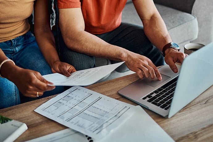 couple sitting on couch working on laptop with papers in front of them