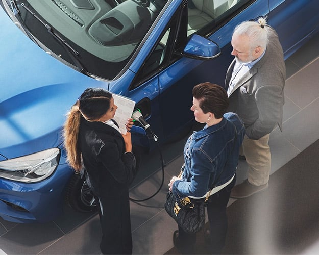 Car salesman selling a couple an electric vehicle in a dealership.