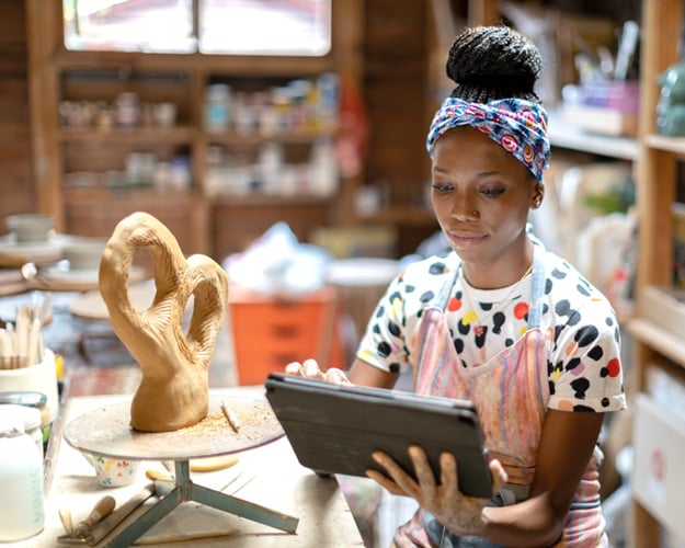 Small business owner of a pottery studio working on tablet.