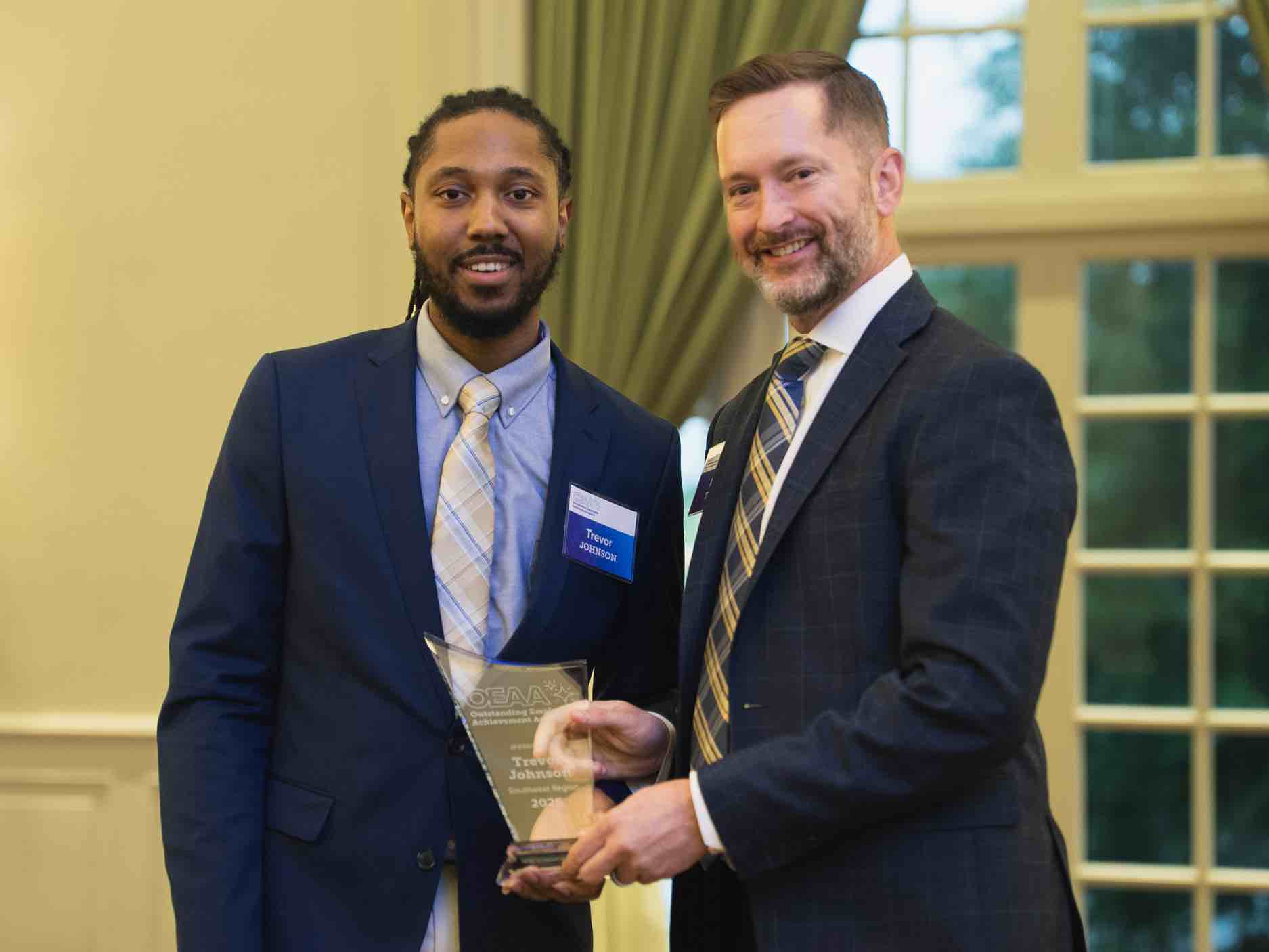 Trevor Johnson receives an OEAA Outstanding Achievement award during a professional ceremony, holding a glass plaque alongside a presenter, recognizing excellence and leadership in rehabilitation health care services.