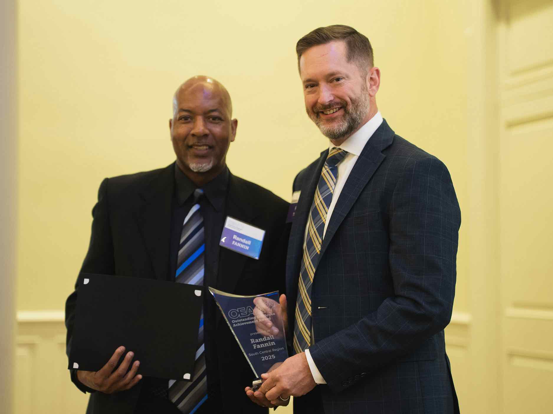 Randall Fannin receives an OEAA Outstanding Achievement award during a professional ceremony, holding a glass plaque alongside a presenter, recognizing excellence and leadership in rehabilitation health care services.