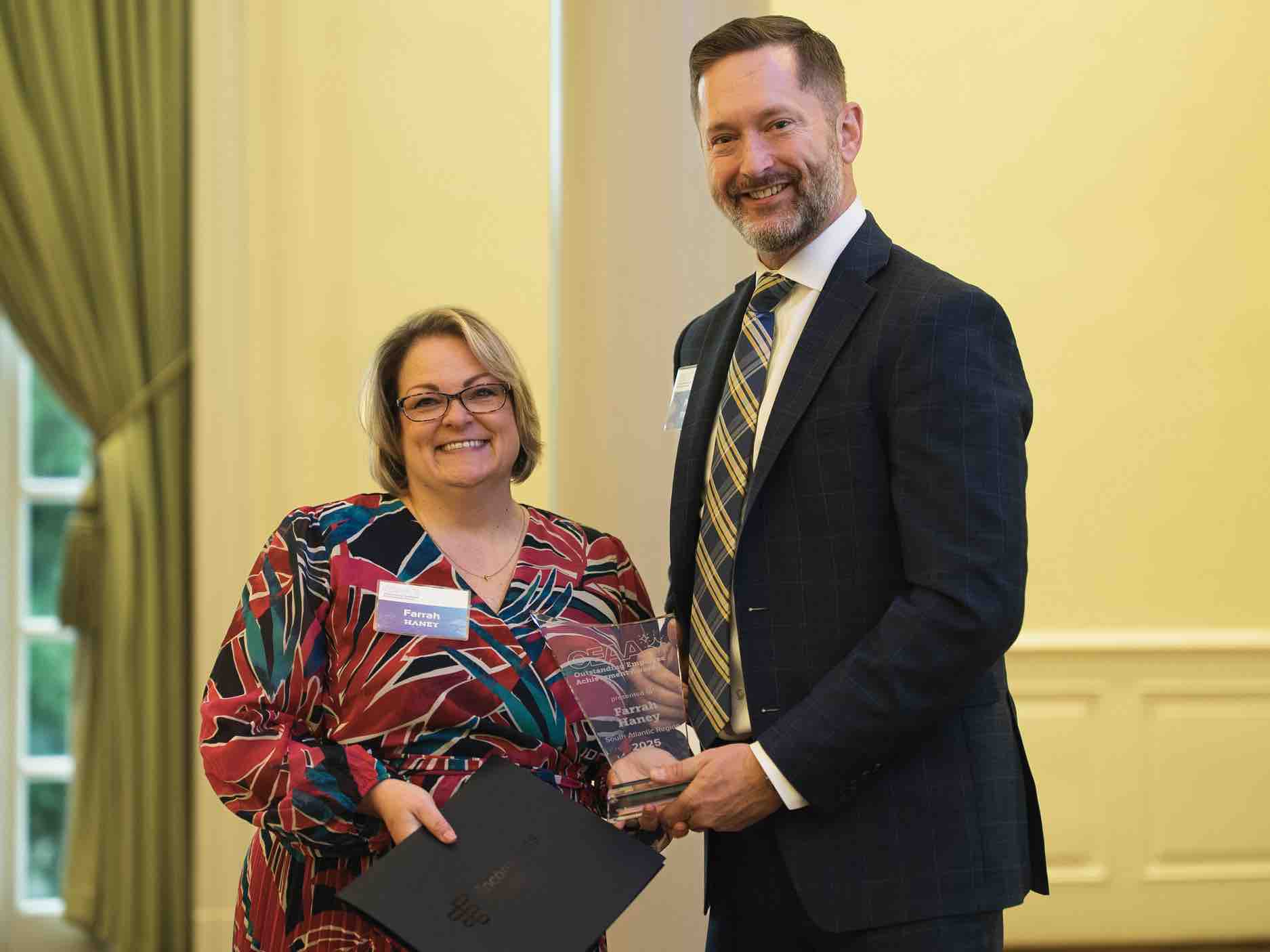 Farrah Haney receives an OEAA Outstanding Achievement award during a professional ceremony, holding a glass plaque alongside a presenter, recognizing excellence and leadership in rehabilitation health care services.