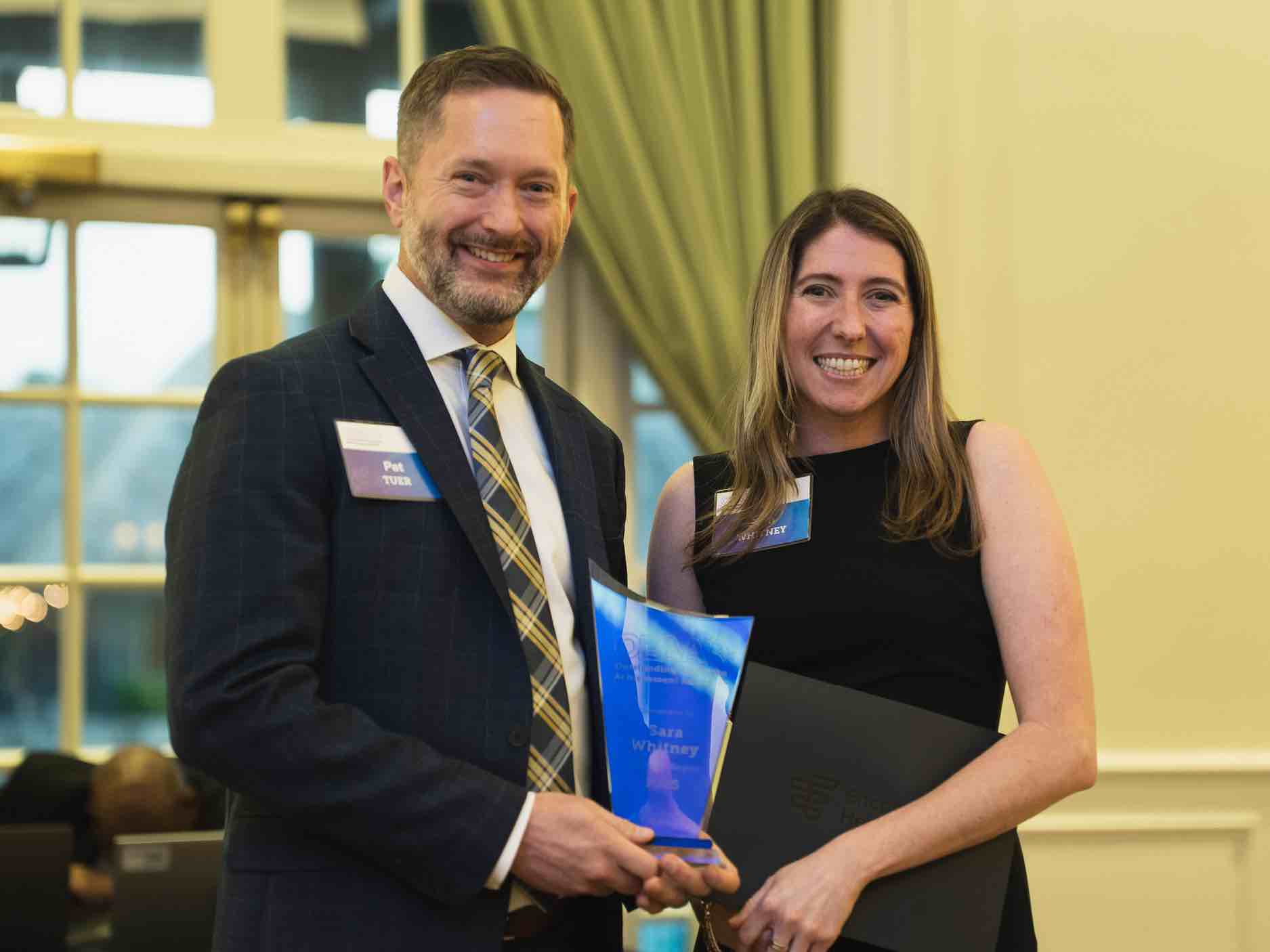 Sara Whitney stands at an OEAA awards presentation, holding a recognition plaque alongside a colleague, representing leadership and excellence in rehabilitation health care achievement and service.