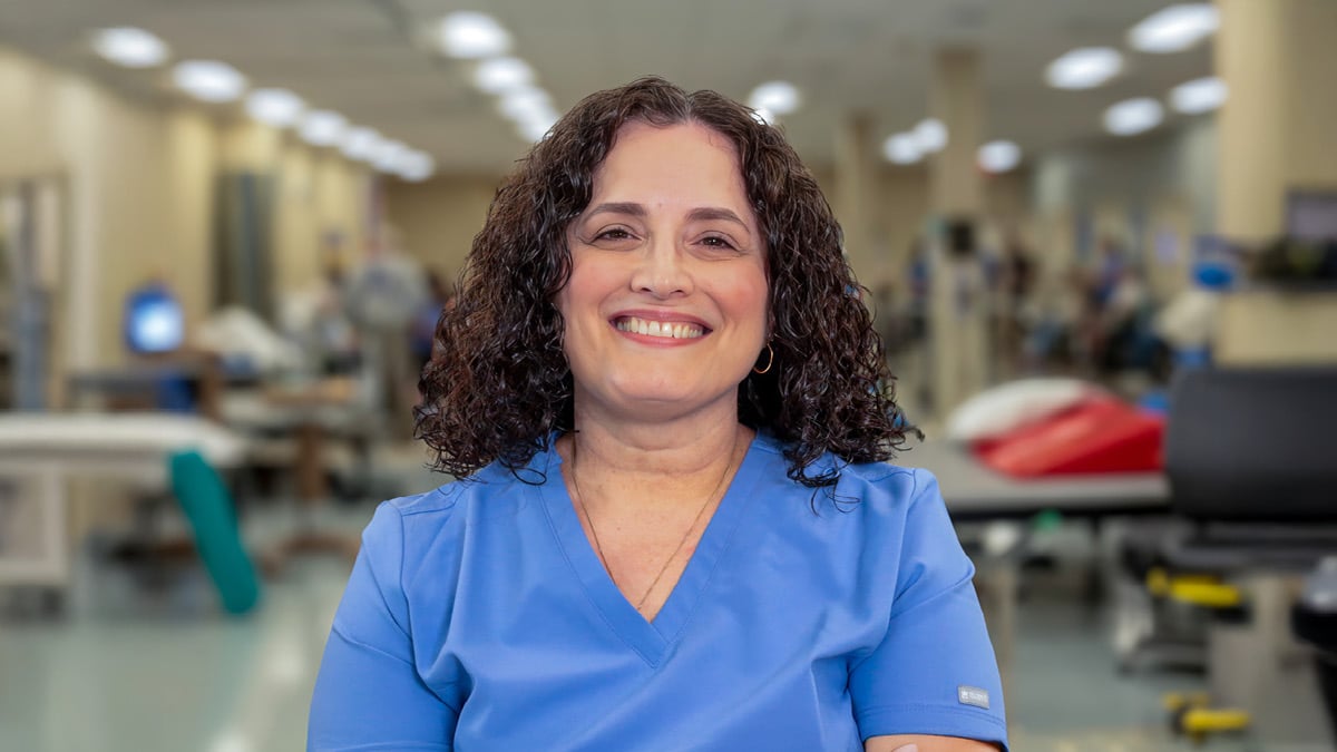 Rehabilitation hospital employee Evangelina Badell recognized as OEAA Southeast winner, pictured in scrubs within a therapy gym environment representing clinical leadership and staff achievement.