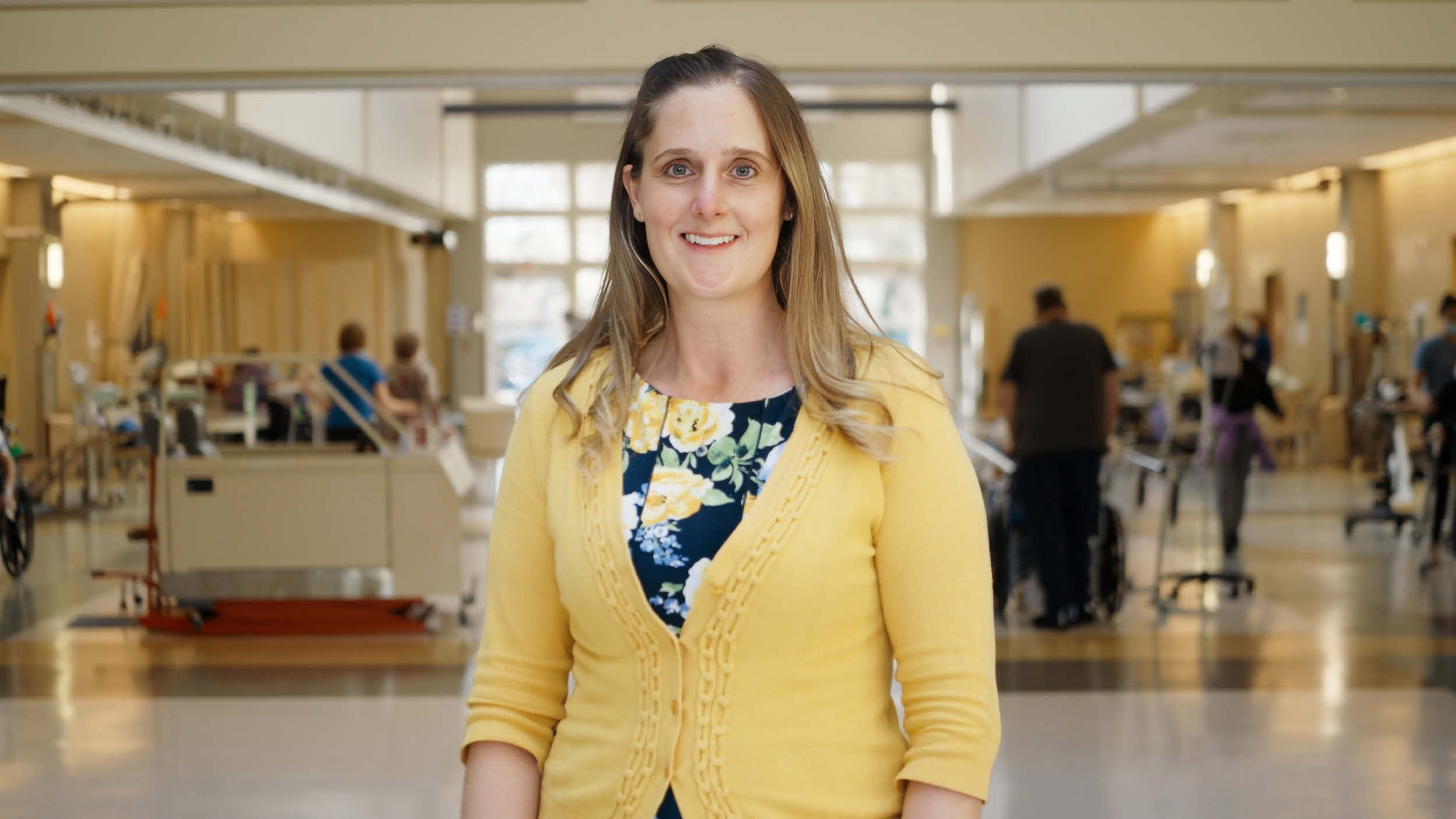 Rehabilitation hospital employee Jennifer Illuminati recognized as OEAA MidAtlantic winner, pictured in a yellow cardigan and floral dress within a hospital environment representing clinical leadership and staff achievement.
