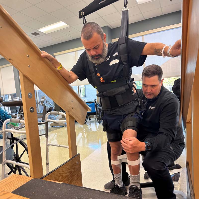 Encompass Health patient ascending stairs while using Aretech ZeroG 3D with an inpatient physical therapist