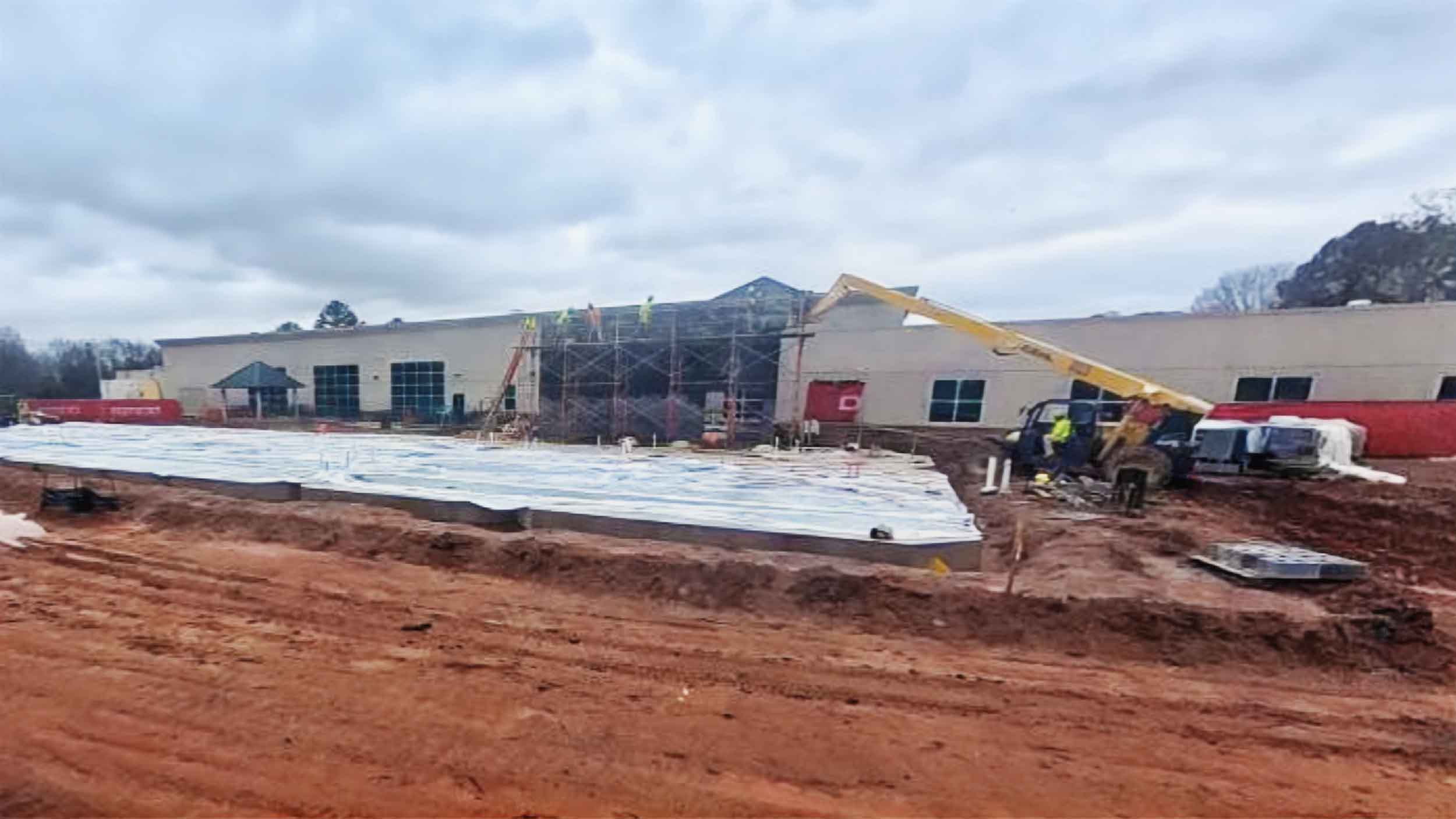 A wide view of AnMed’s new construction site showing scaffolding, foundation work, heavy equipment, and exterior building walls in progress on a muddy jobsite.