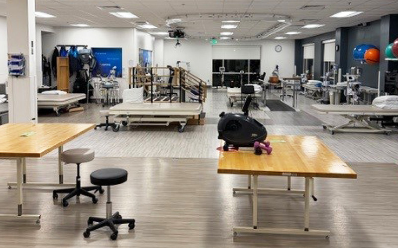 Wide view of the UVA therapy gym expansion showing treatment tables, therapy stairs, exercise equipment, and open floor space designed for rehabilitation activities.