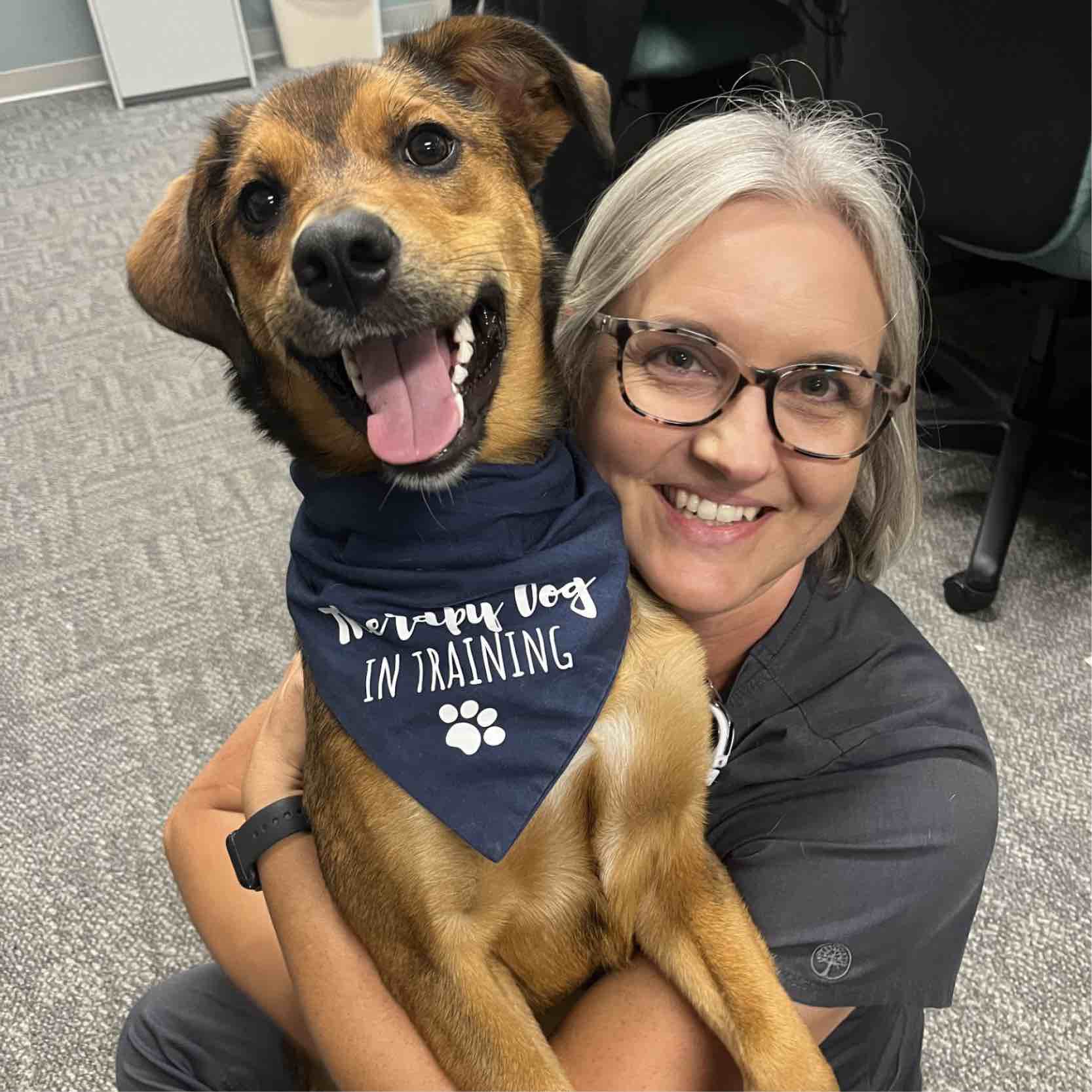 Rehabilitation hospital staff member in Greenville holds a therapy dog during a pet therapy visit, demonstrating supportive interactions that enhance patient-centered care.