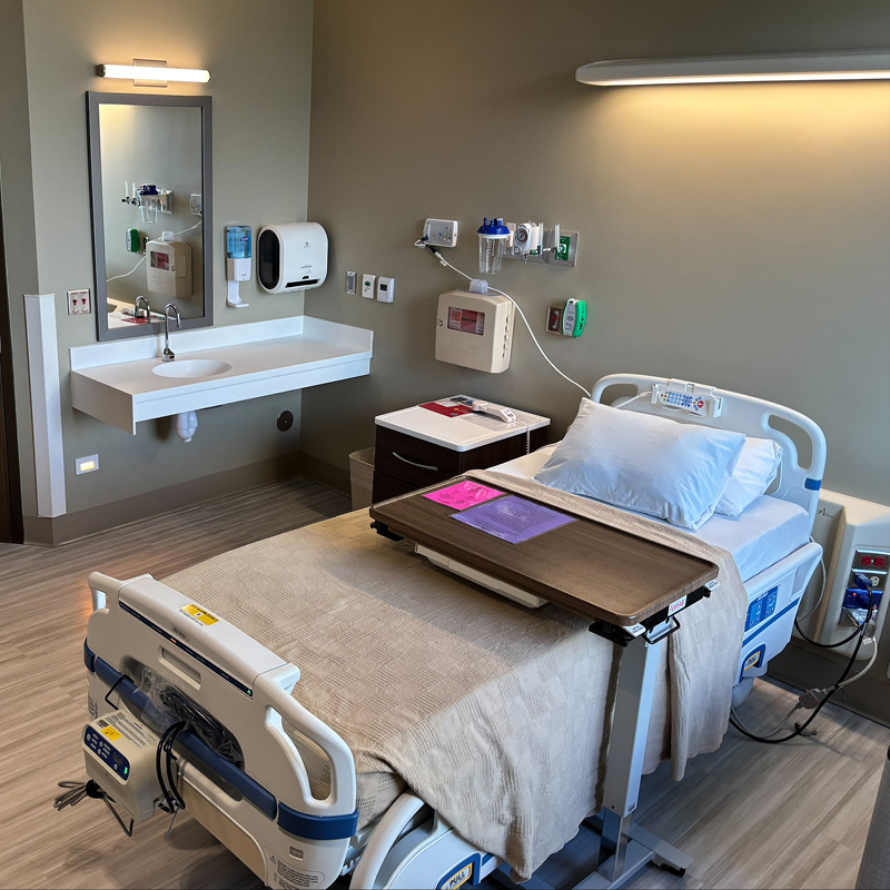 Hospital room with a neatly made bed, adjustable tray table, and modern medical equipment. Clean, organized, and calm atmosphere.