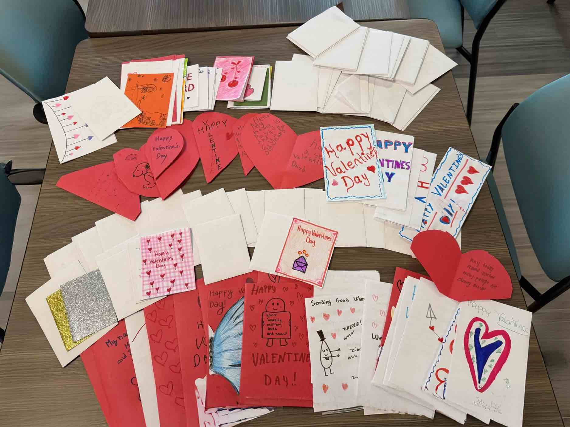 A table covered with colorful handmade Valentine’s Day cards from Monteverde Academy, featuring hearts, drawings, messages, and stacked blank envelopes.