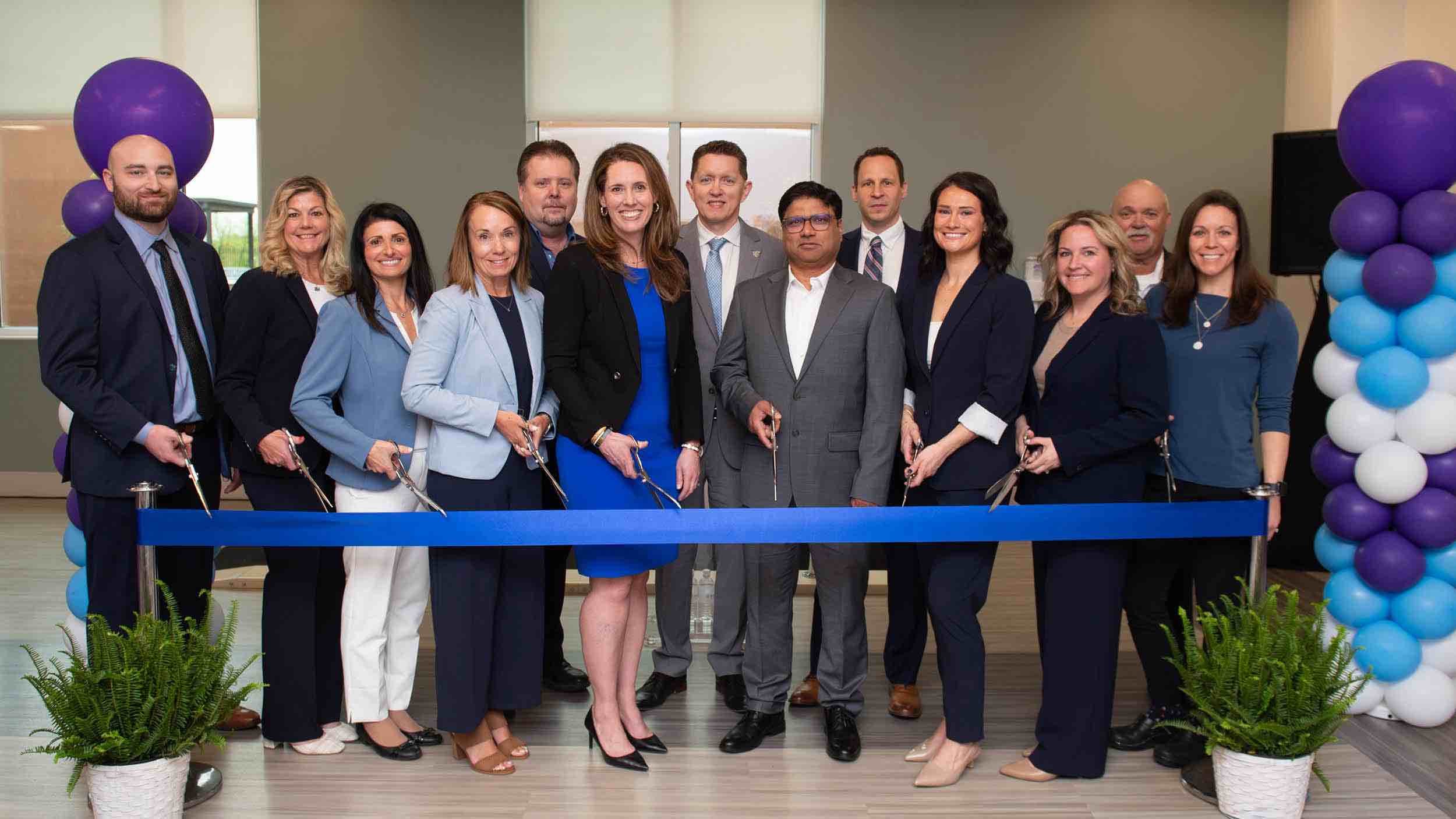 Leadership team and community partners participate in a Concordville ribbon cutting ceremony at a rehabilitation hospital, standing behind a blue ribbon with balloons marking a facility opening.