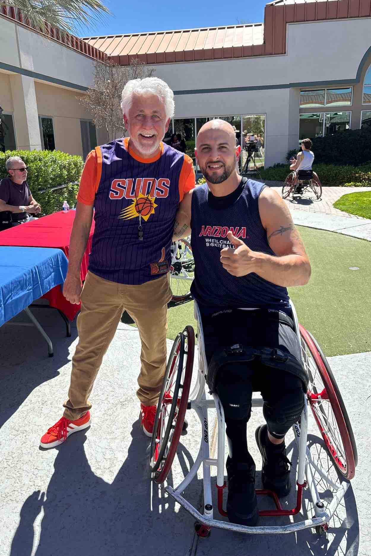 A wheelchair basketball athlete poses with a coach outdoors at a rehabilitation hospital, representing mentorship, adaptive sports participation, and recovery-focused programs supporting strength and independence.