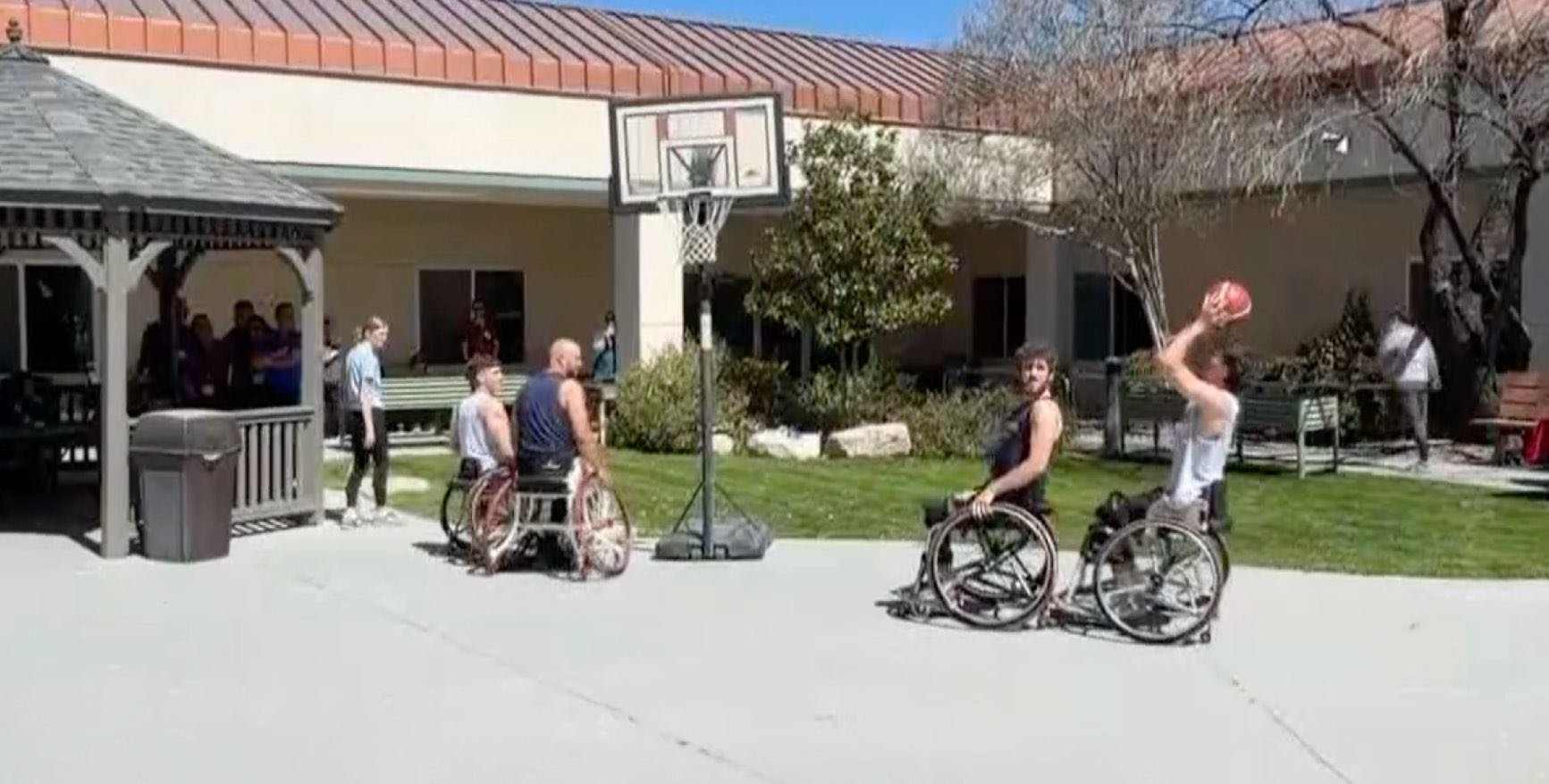 Individuals using sport wheelchairs participate in wheelchair basketball outside a rehabilitation hospital, demonstrating adaptive athletics, teamwork, and therapeutic recreation that supports mobility and recovery.
