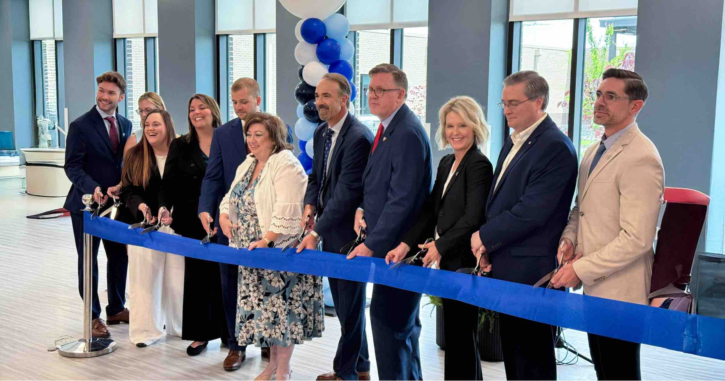 Piedmont Healthcare Encompass Health Eastside Rehabilitation Hospital ribbon cutting ceremony with leaders holding scissors behind a blue ribbon in a modern lobby