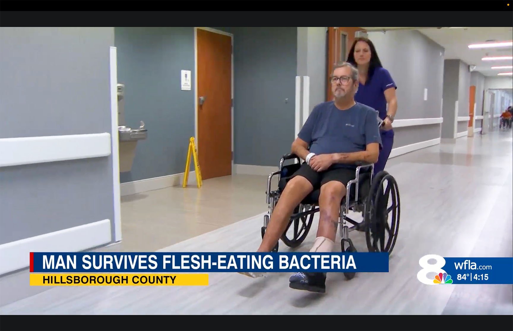 Man in a wheelchair, pushed by a woman in scrubs, in a hospital hallway. Caption reads, "Man survives flesh-eating bacteria, Hillsborough County."