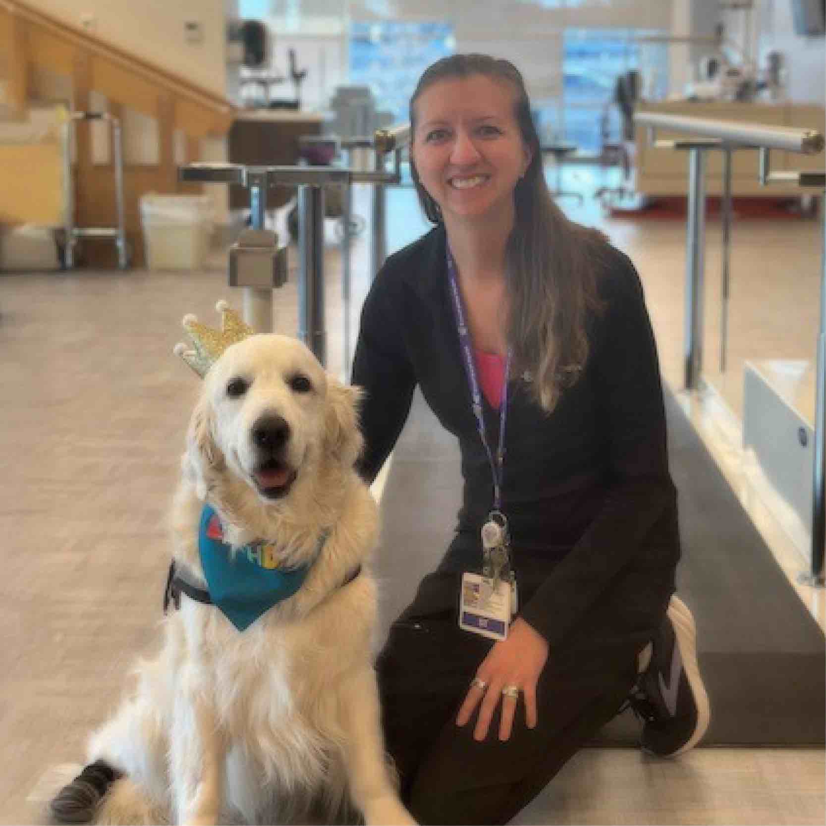 A therapy dog sits beside a rehabilitation team member in a bright therapy gym, highlighting the benefits of pet therapy for patient motivation and emotional support.