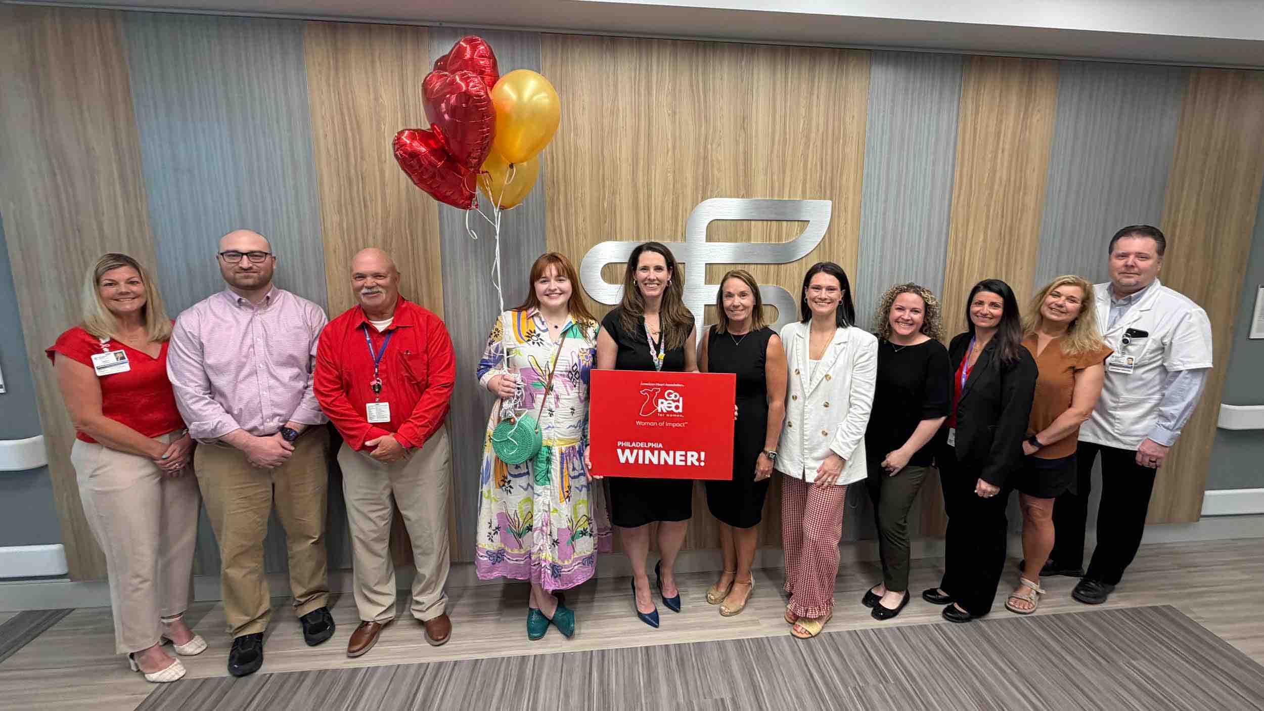 Healthcare team stands in a row holding Go Red for Women winner sign with balloons, promoting stroke awareness, cardiovascular health, and rehabilitation-focused community recognition event