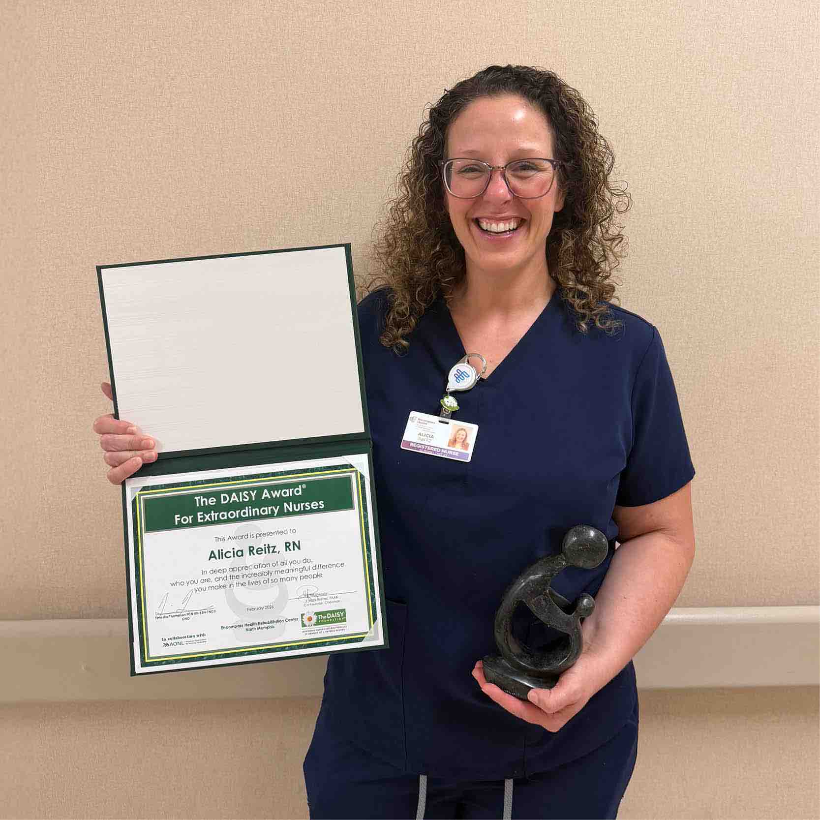 Healthcare professional holds DAISY Award certificate and sculpture, recognizing excellence in patient care, nursing leadership, and rehabilitation services within a hospital setting