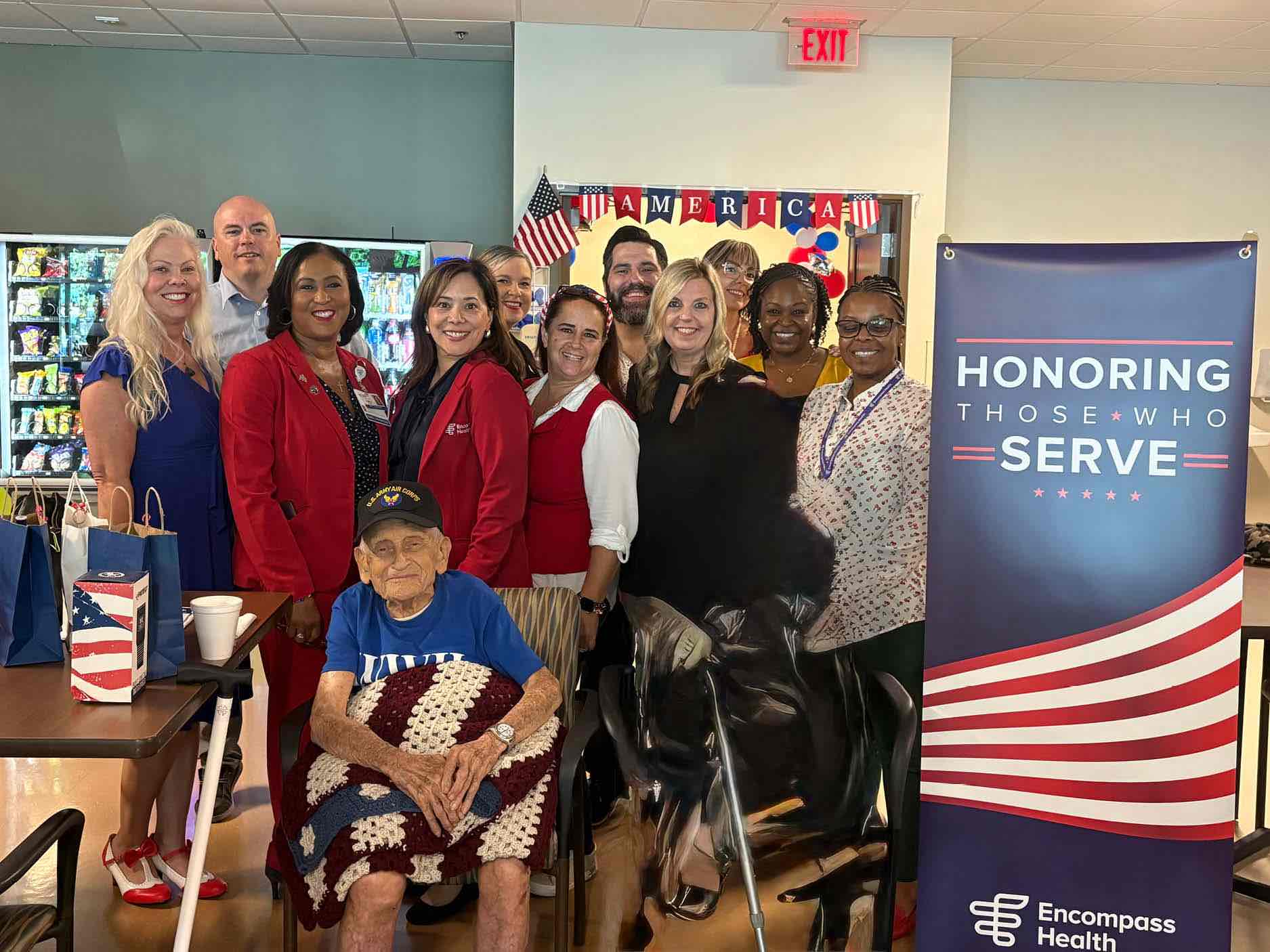 Veteran is recognized during a community appreciation event at an inpatient rehabilitation hospital, surrounded by staff and partners honoring veterans and military service.